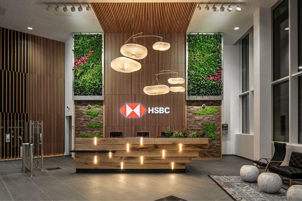A modern HSBC reception area with a wooden desk, hanging lights, vertical garden walls, and the HSBC logo displayed behind the desk. The space features sleek decor and a welcoming atmosphere.