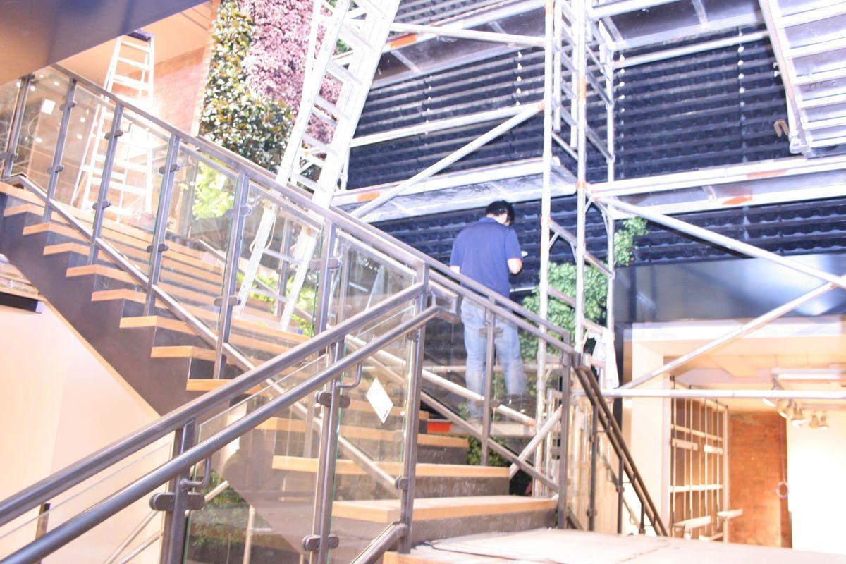 A person installing a green wall system in a brightly lit, industrial-style building featuring metal beams and exposed brick walls.