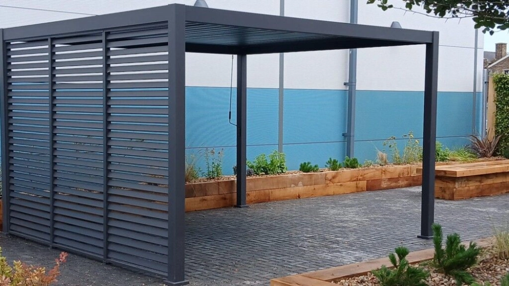 Pergola in the centre of the image with wooden plant boxes fencing the parameter of the outside area