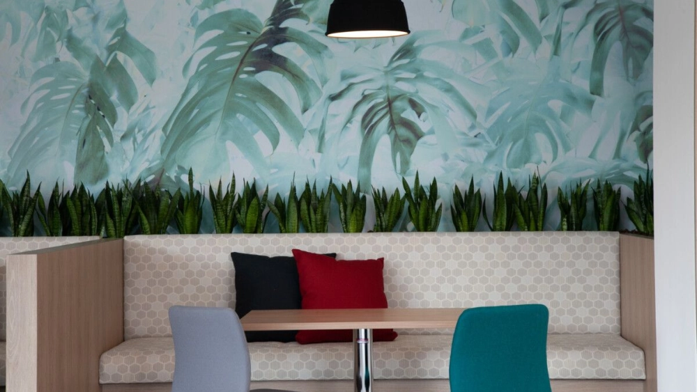Two pillows on a bench next to a wall with wallpaper of plants