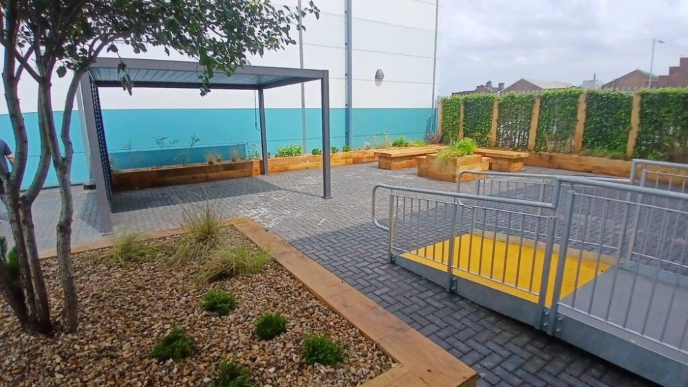 tree to the left hand side in a wooden planter box and a ramp to the right hand side going into the outdoor space