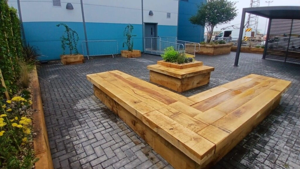 L-shaped wooden bench next to a planter box with a shrub in it