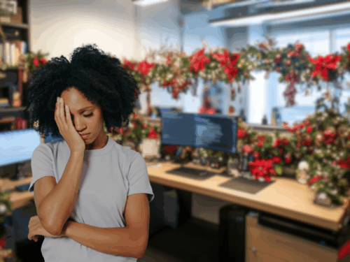 A woman stands in an office decorated with Christmas garlands and red bows, looking stressed with her hand on her face. Computer monitors and workstations are visible in the festive background.